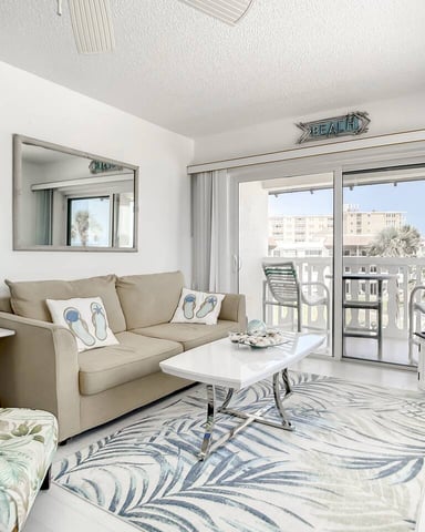 Beachfront hotel room with ocean view through glass doors, balcony seating, and potted plants
